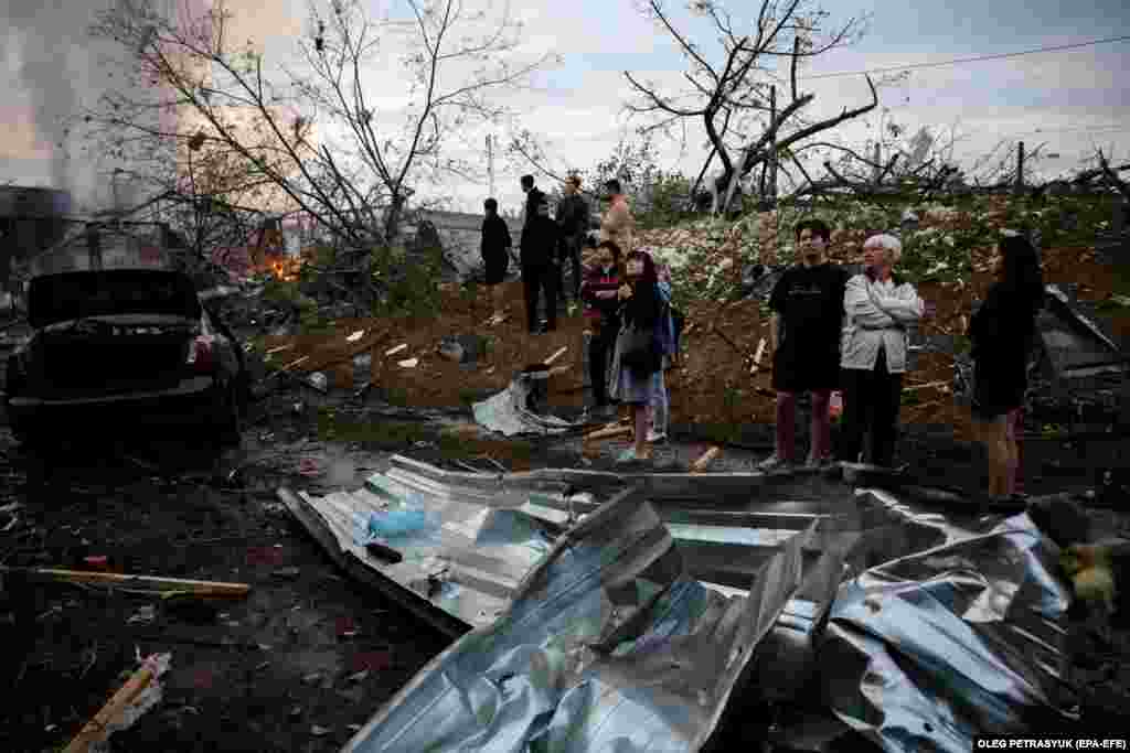 Residents stand near the site of a missile attack in Kyiv as fires burn in the background. The Ukrainian Air Force claimed it had intercepted 36 of 43 cruise missiles launched deep into Ukraine.