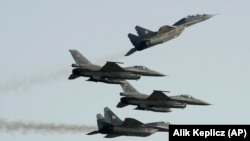 Два истребителя МиГ-29 российского производства, принадлежащих ВВС Польши, пролетают над и под двумя истребителями F-16 ВВС США во время авиашоу в Радоме, Польша, 27 августа 2011 года.