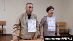 Гражданские активисты Маруа Ескендирова и Амангельды Оразбаев на суде по их делу с плакатами, на которых перечислены сутки, в которые они в разное время отбывали административные аресты. Уральск, 7 октября 2022 года