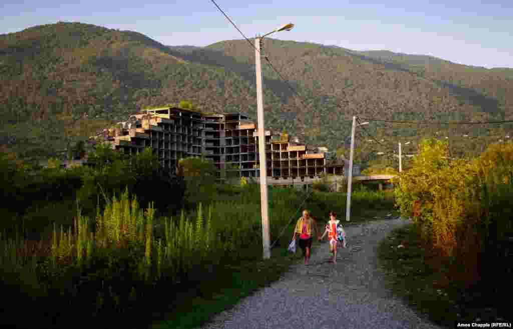 A Russian father and daughter walking to the beach at Gagra. An abandoned building site is in the background. 