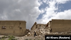 په ګیان ولسوالۍ کې یو کس په زلزله کې د زیانمنو کورونو تر څنګ تېرېږي - د جون ۲۳مې انځور.