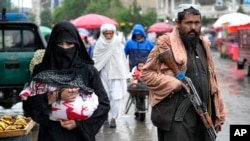 Viața la Kabul: o femeie afgană merge la piață în ținuta obligatorie, în timp ce un luptător taliban stă de pază (arhivă). 
