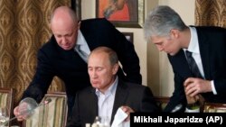 Евгений Пригожин (слева) помогает Владимиру Путину во время ужина с иностранными учеными и журналистами в ресторане Cheval Blanc. 11 ноября 2011 года