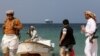 Armed men stand on the beach as the Galaxy Leader commercial ship, seized by Yemen's Huthis in November, is anchored off the coast of Salif.