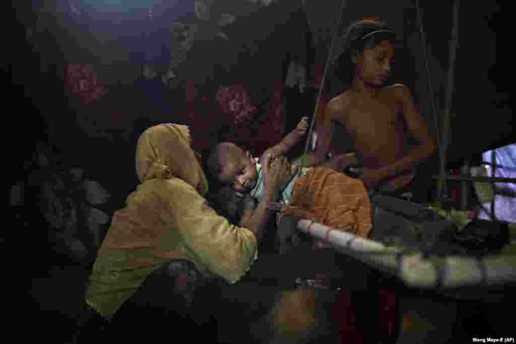 O fiică (dreapta) își predă fratele mamei lor „M” în adăpostul lor din lagărul de refugiați Kutupalong din Bangladesh. „M” a fost violată de șase soldați din forțele de securitate din Burma, după ce i-au strangulat fiul de doi ani. Mai târziu, „M” a aflat că este însărcinată și că va naște un băiat. După ce i-a spus soțului ei ce s-a întâmplat, acesta a învinuit-o pentru viol și a părăsit-o. (AP / Wong Maye-E)